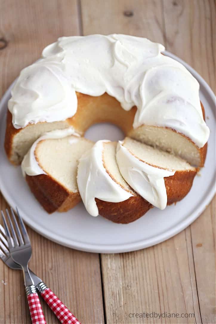 a bundt cake with white frosting on a plate next to a fork and knife