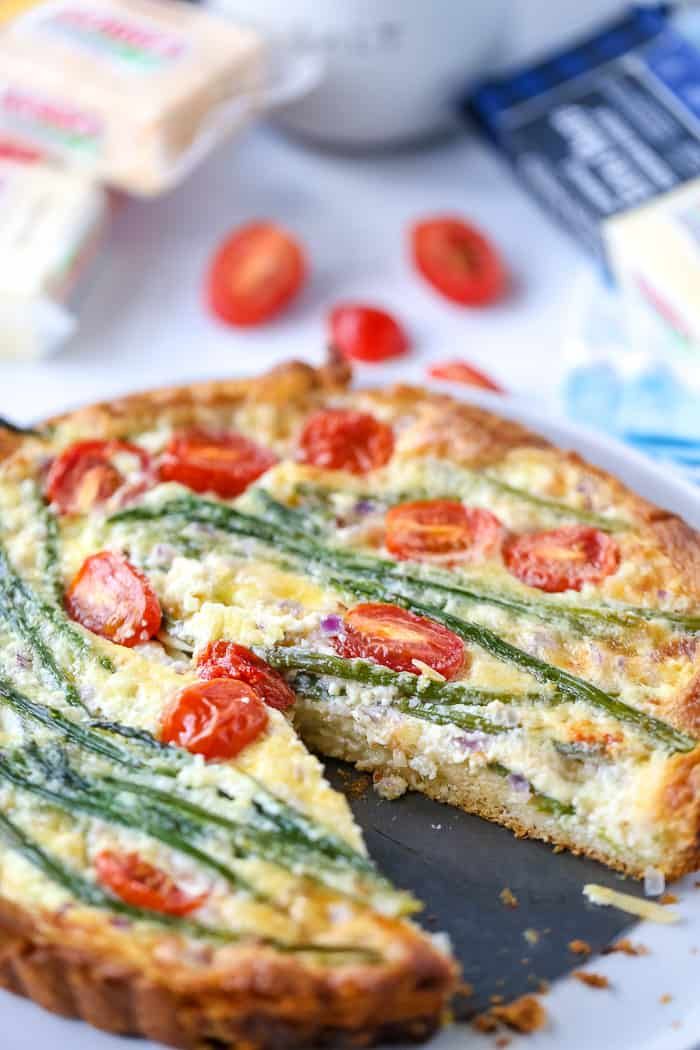 a quiche with tomatoes and asparagus is cut in half on a plate