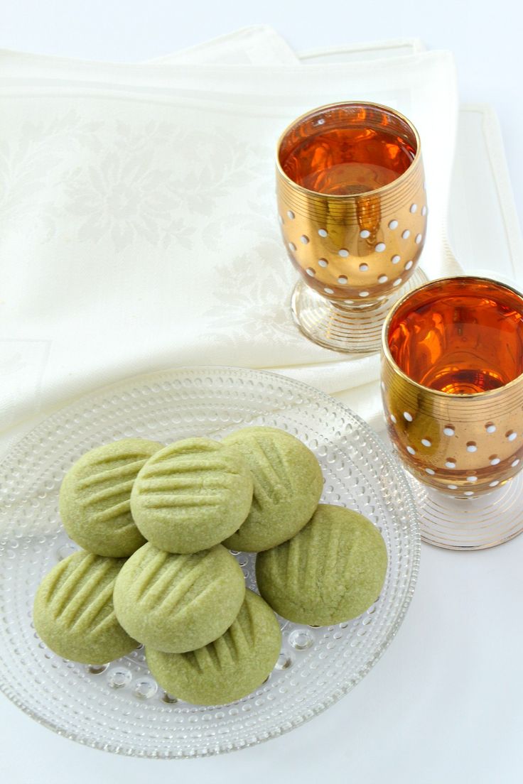 some green cookies are on a plate next to two glasses and a gold tea cup