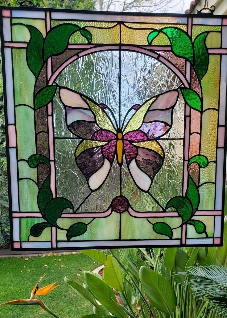 a stained glass window with green leaves and a butterfly on it's side in the grass