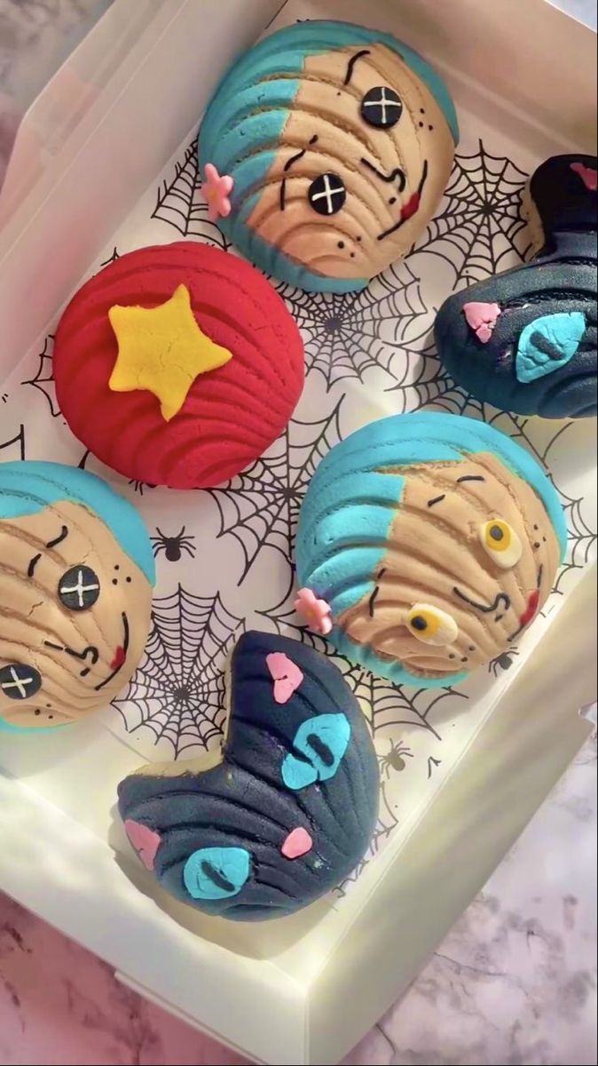 four decorated cookies in the shape of faces on a tray with spider webs around them