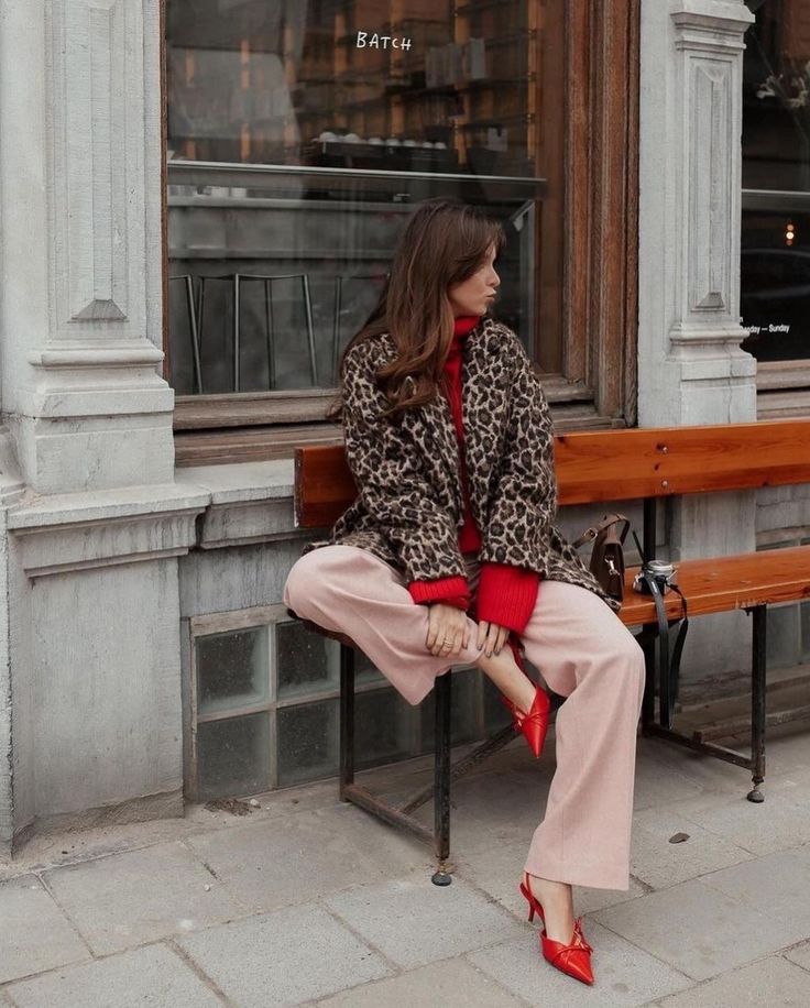 a woman sitting on a bench in front of a store window wearing leopard print coat