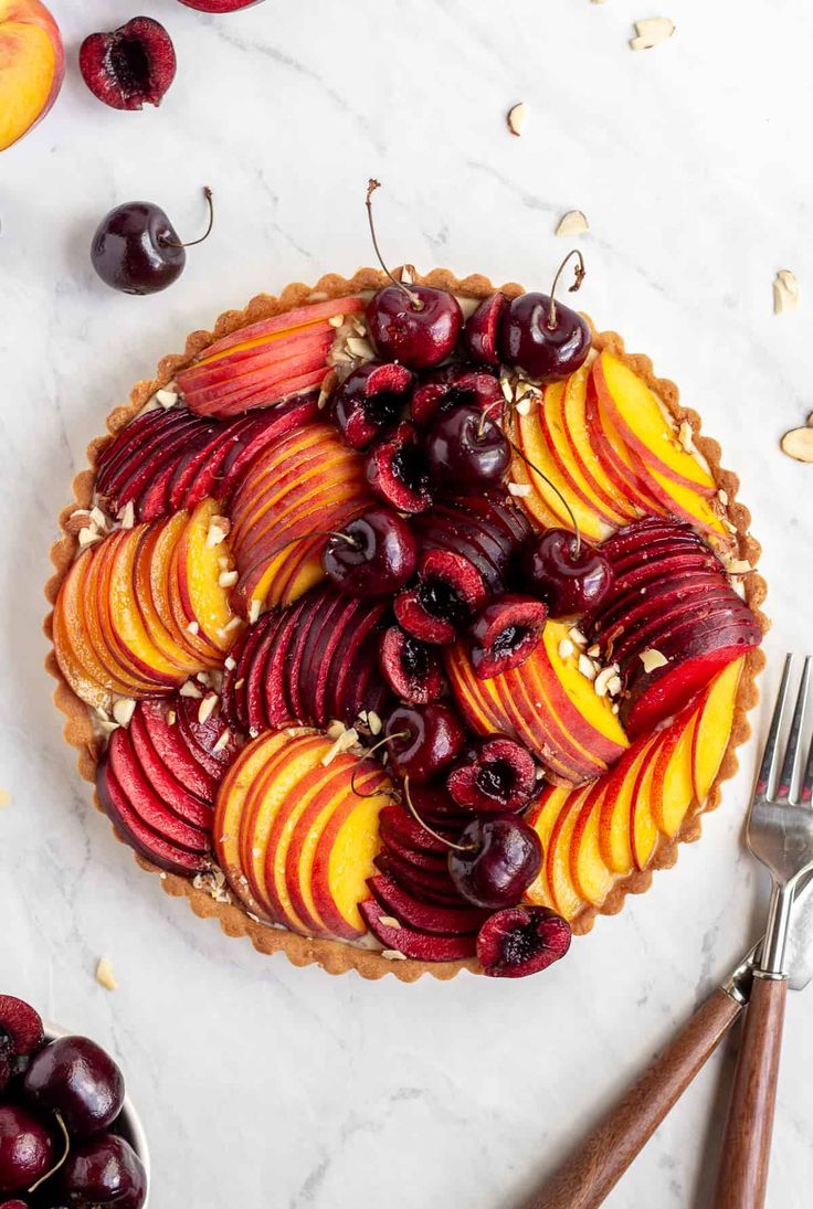 a pie topped with sliced peaches and cherries on top of a white table