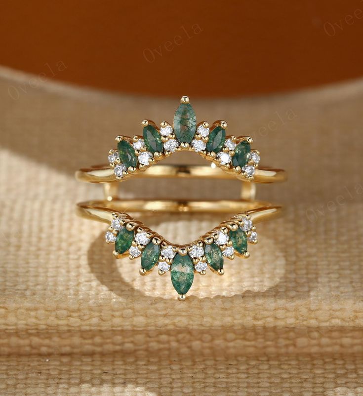 two gold rings with green and white stones on top of each other in front of a beige cloth