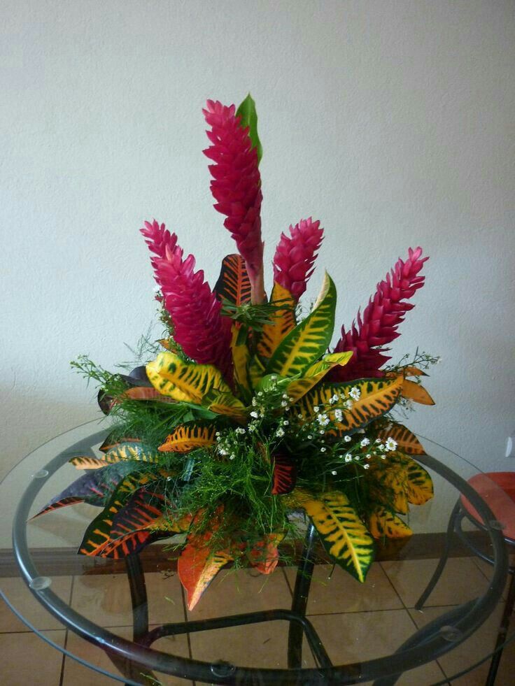 a glass table topped with a vase filled with flowers and greenery next to a wall