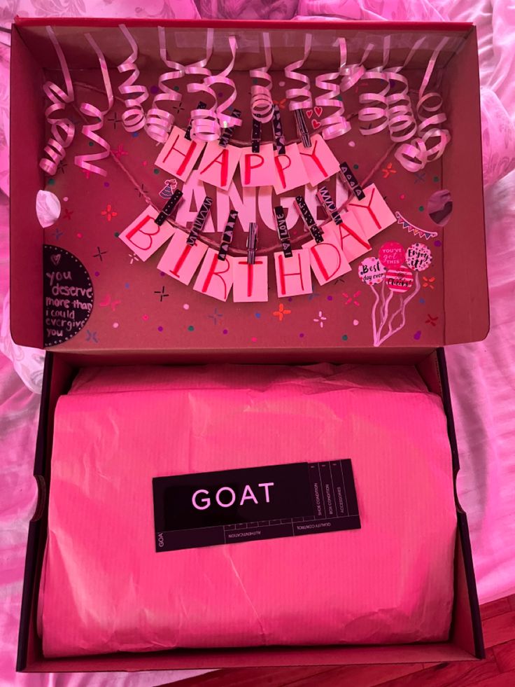 a pink gift box with the word goat on it and some decorations in front of it