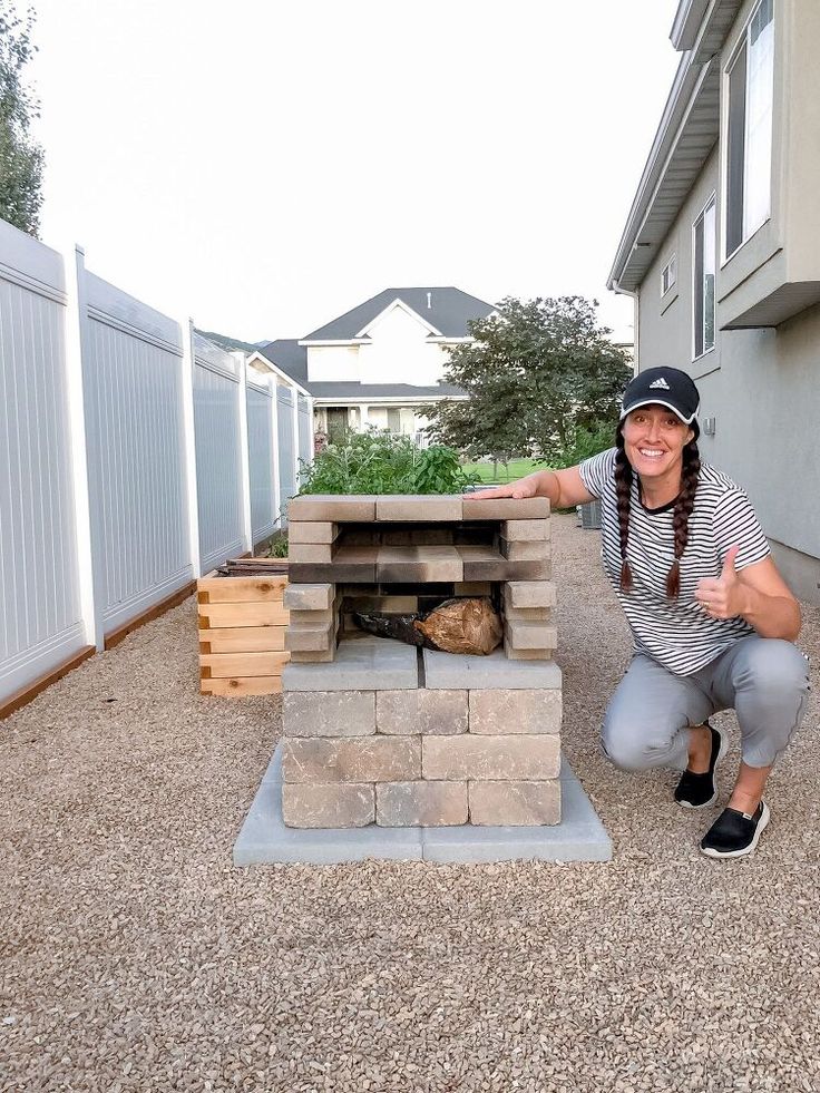 a woman kneeling down in front of a fire pit made out of bricks and wood