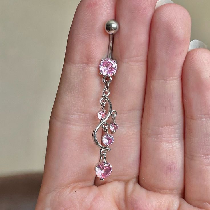 a person is holding a pink jeweled navel bar in their left hand,