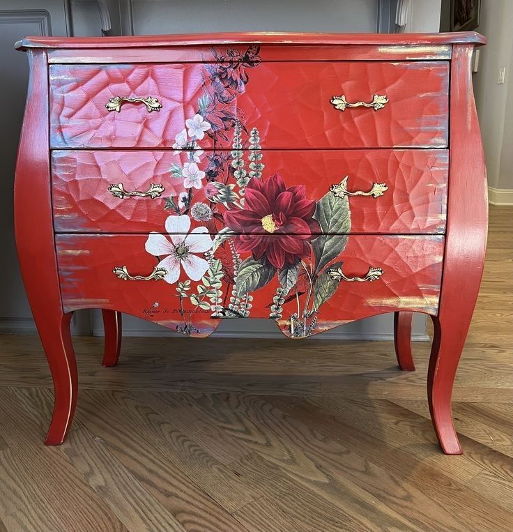 a red dresser with flowers painted on the front and sides, sitting on a hard wood floor