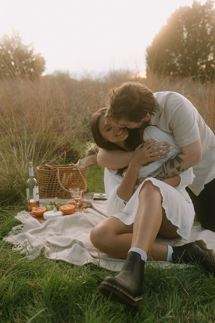 a man and woman sitting on top of a grass covered field next to each other