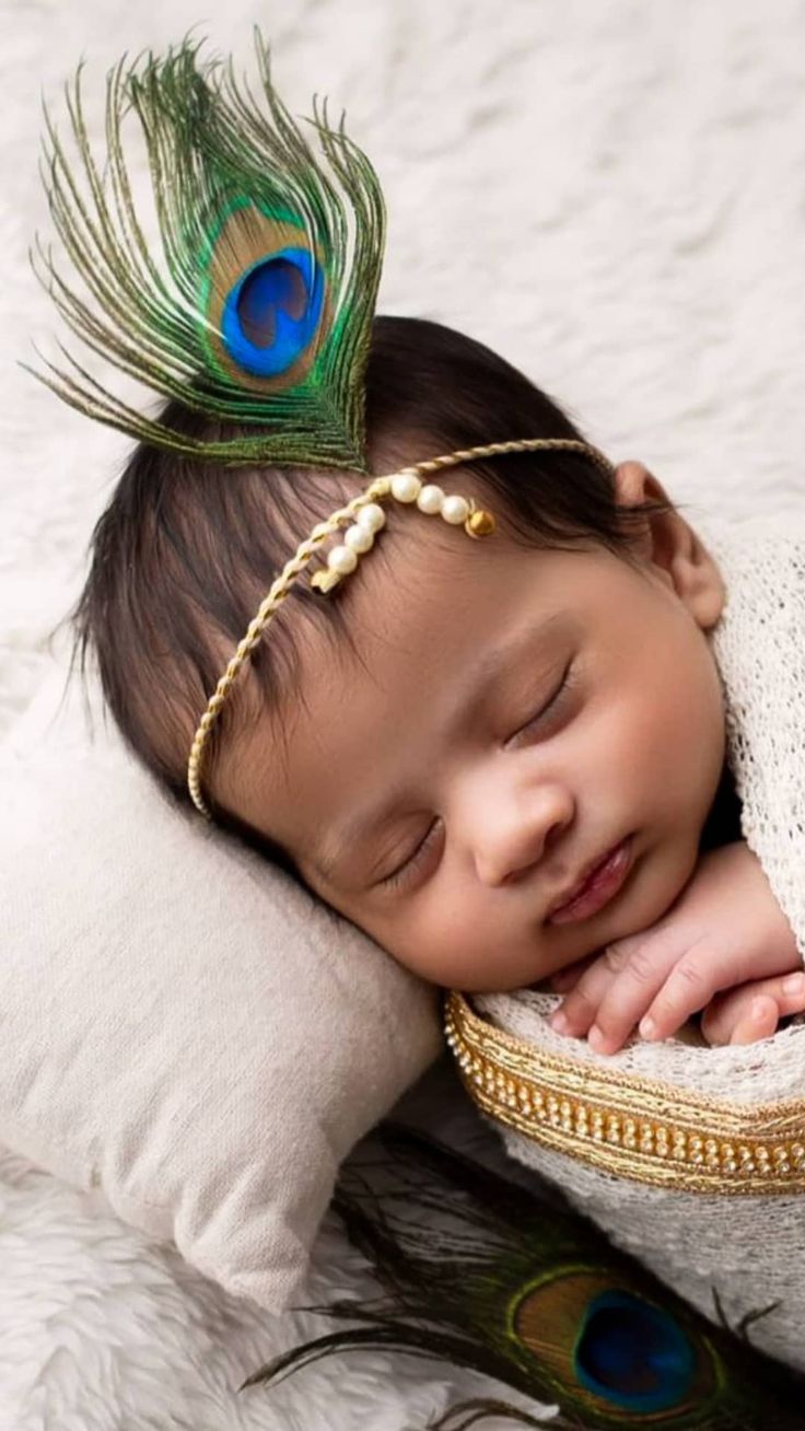 a baby sleeping on top of a white pillow with a peacock feather headband around it's face