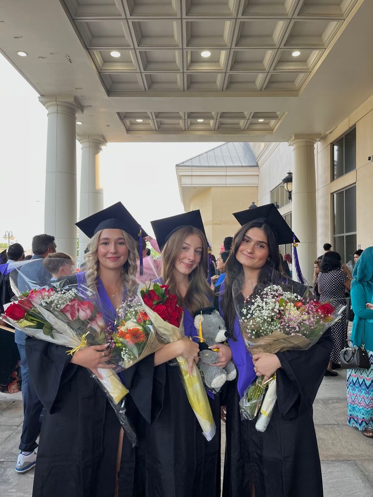 three girls in graduation gowns holding flowers