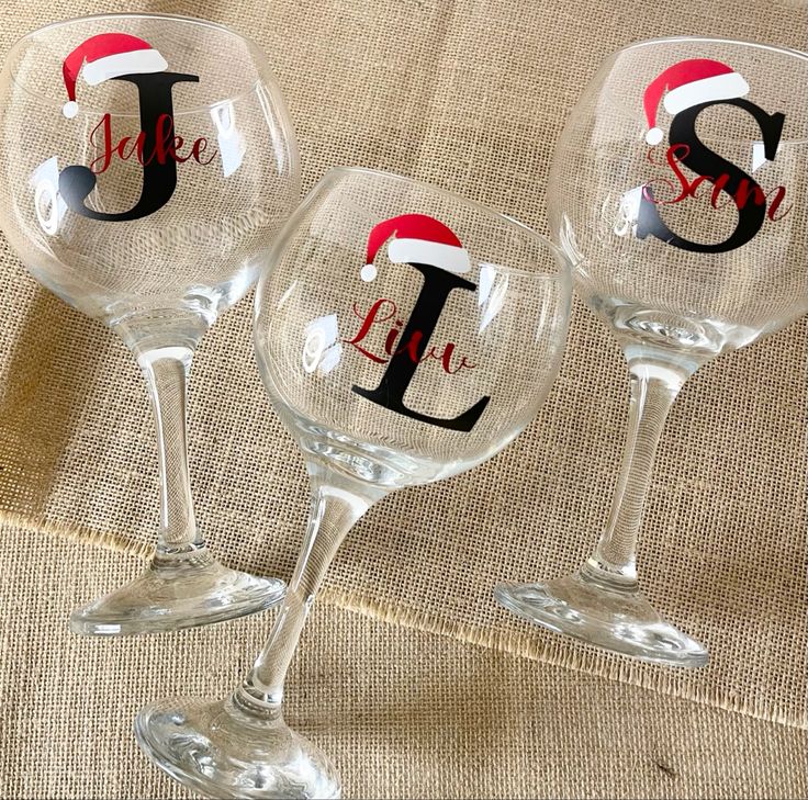 three wine glasses with the letter j and santa's hat on them, sitting next to each other