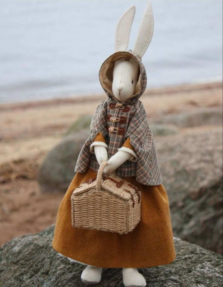 a white rabbit in a brown dress holding a wicker basket and standing on top of a rock