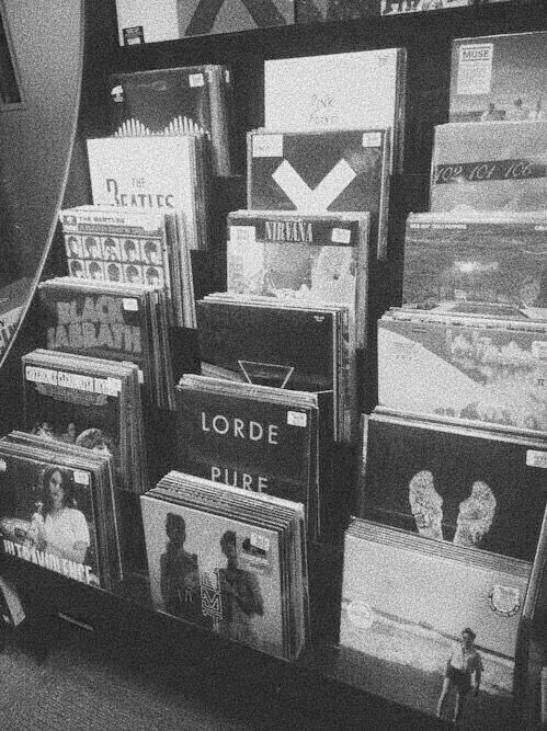 black and white photograph of records on display in a store front window, with one person looking at them