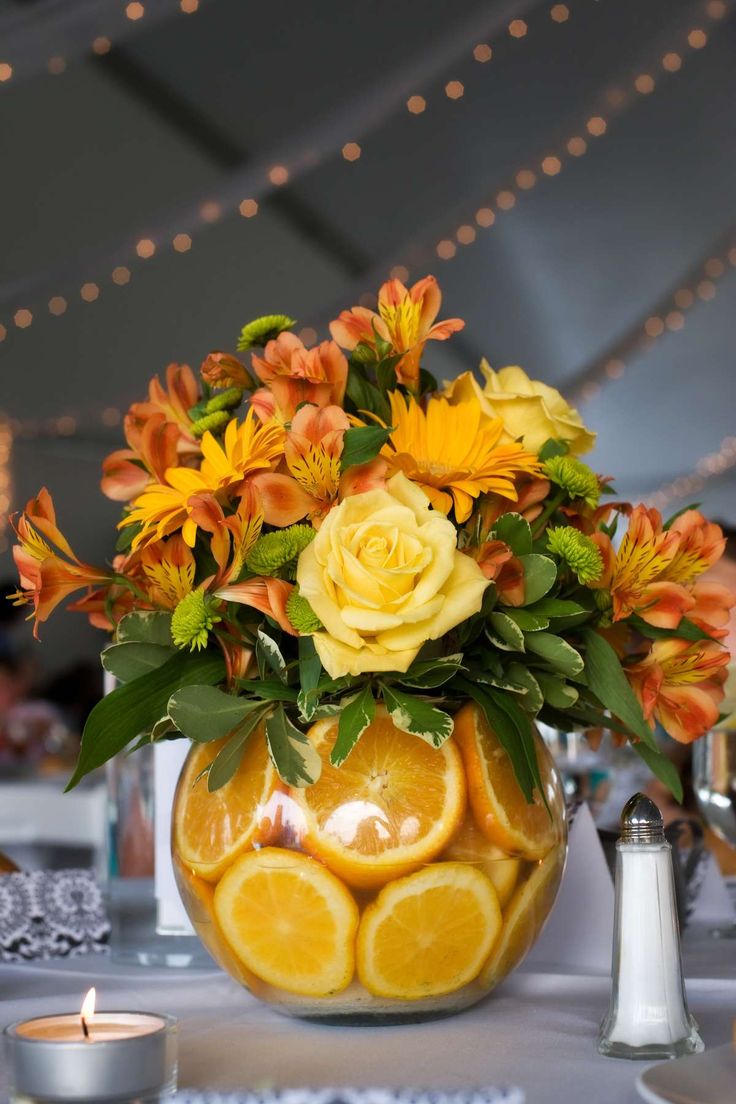 a vase filled with oranges and yellow flowers sitting on top of a white table