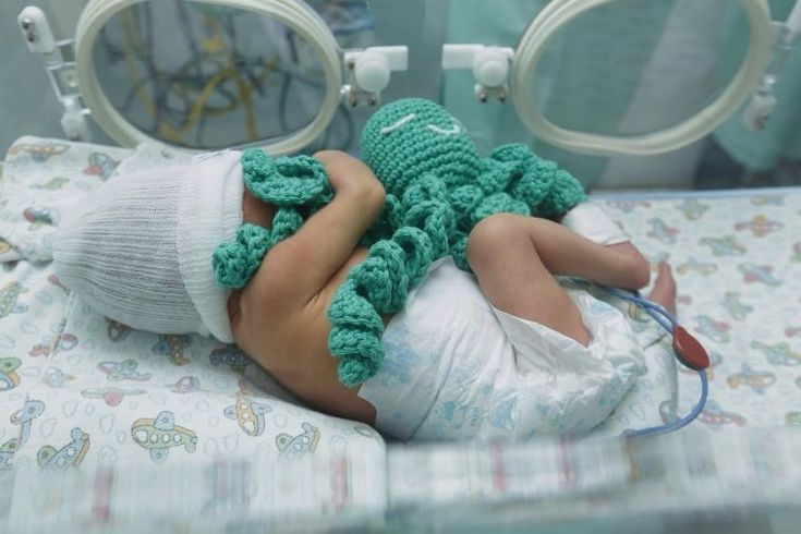 a small child laying in a hospital bed wearing a green crochet hat and diaper