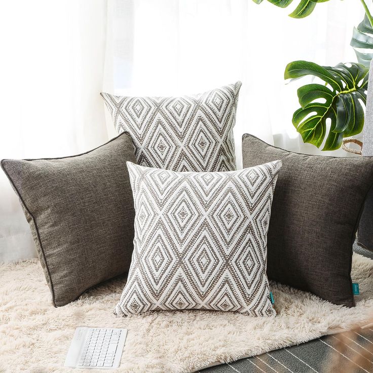 three pillows on a rug next to a computer keyboard and potted plant in front of a window