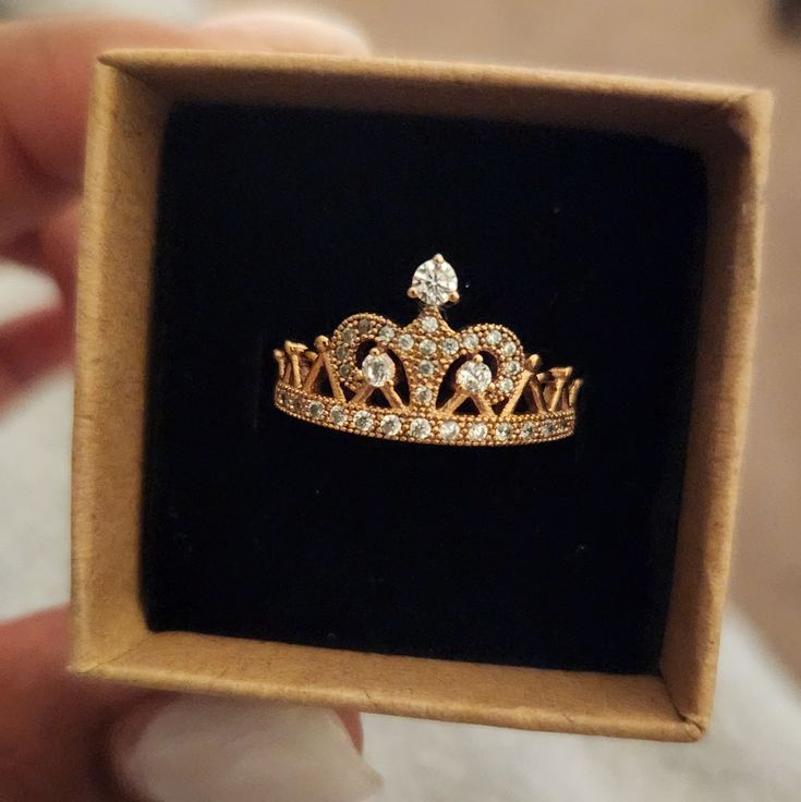 a person holding up a gold and diamond tiara in a black box with its lid open