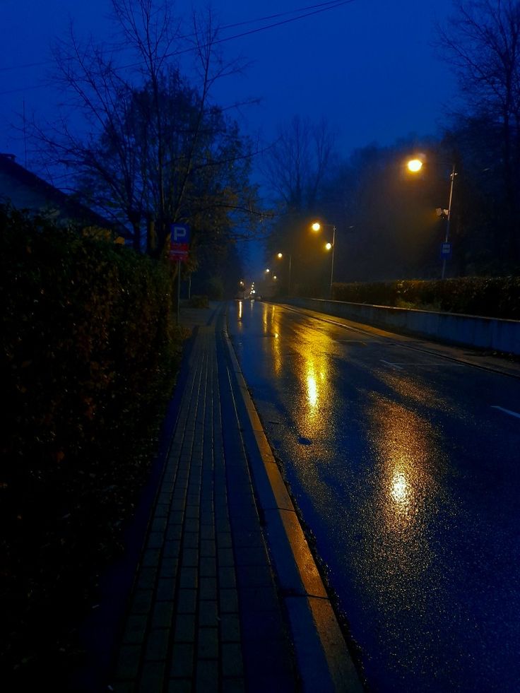 an empty street at night with the lights on and rain coming down from the sky