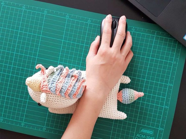 a person holding a cell phone next to a knitted animal on a cutting board