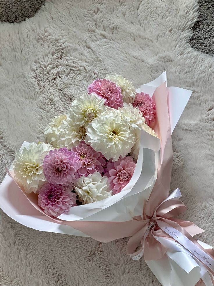 a bouquet of pink and white flowers in a wrapper on a furry surface with a ribbon