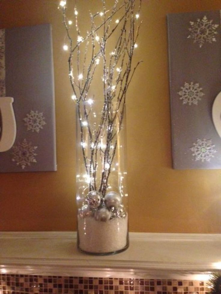 a vase filled with branches and lights sitting on top of a mantel covered in snowflakes