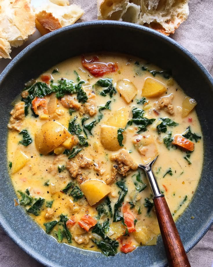 a bowl of soup with meat, potatoes and spinach in it next to bread