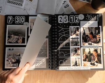 a person is holding an open book on a table with many photos and papers scattered around it