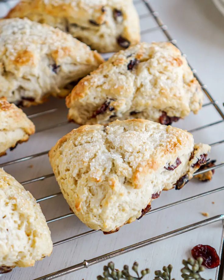 several scones sitting on a cooling rack with cranberries and herbs around them