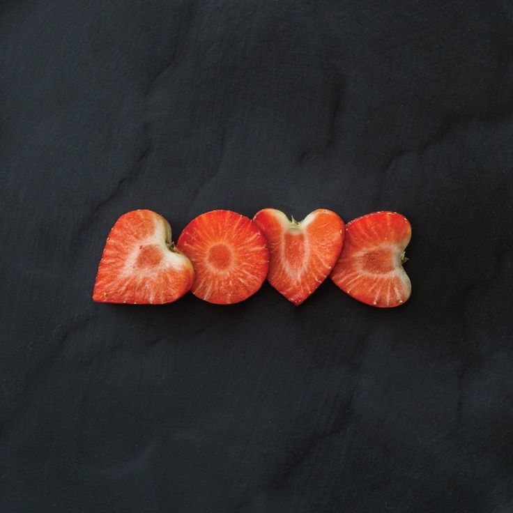 four slices of fruit arranged in the shape of hearts on a black surface with one cut in half