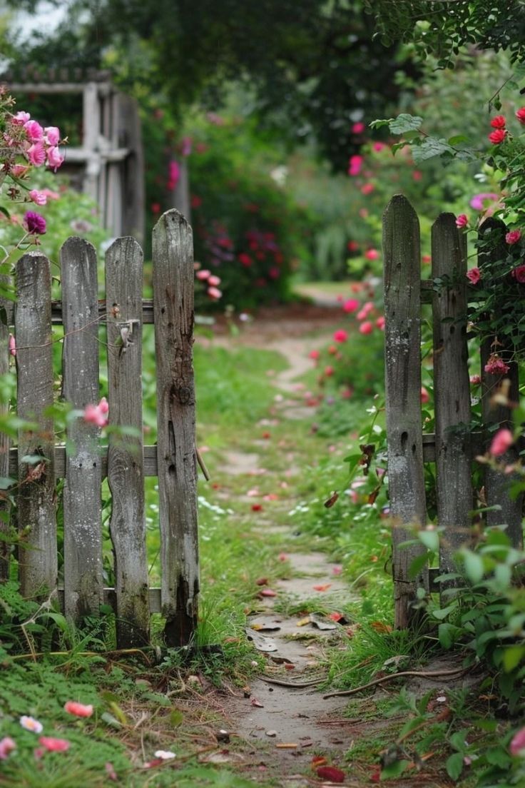 an old wooden fence is surrounded by pink flowers and greenery on the other side