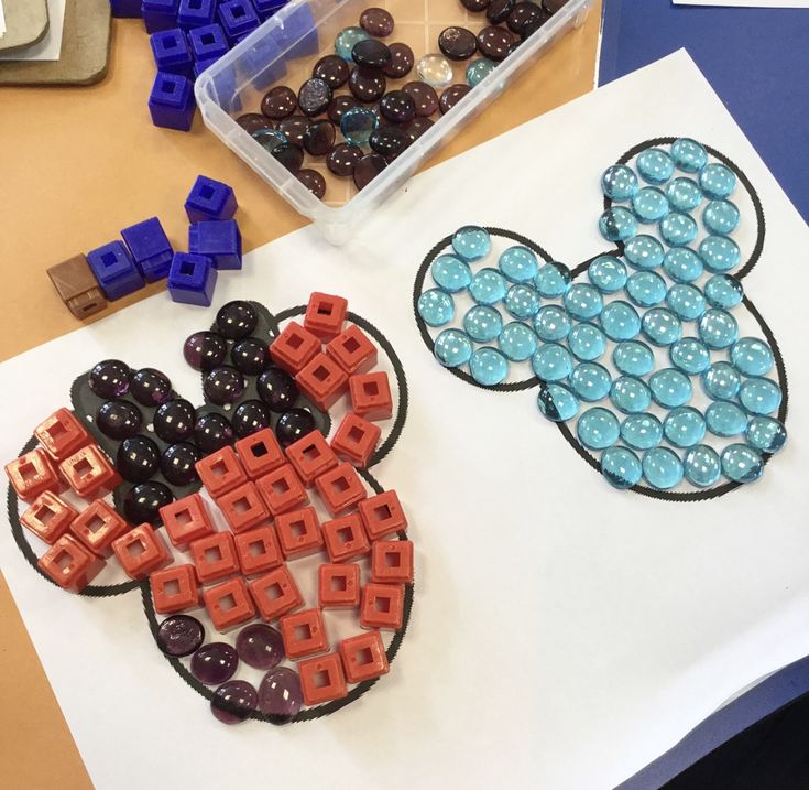 two mickey mouse shaped magnets sitting on top of a white piece of paper next to blue and red beads