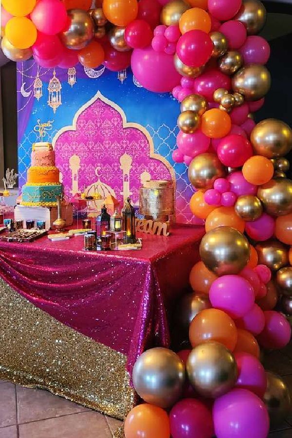 a table topped with lots of balloons next to a purple and gold cake covered in confetti