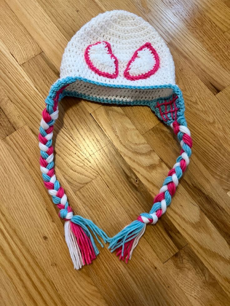 a crocheted hat with hearts and tassels on the side sitting on a wooden floor