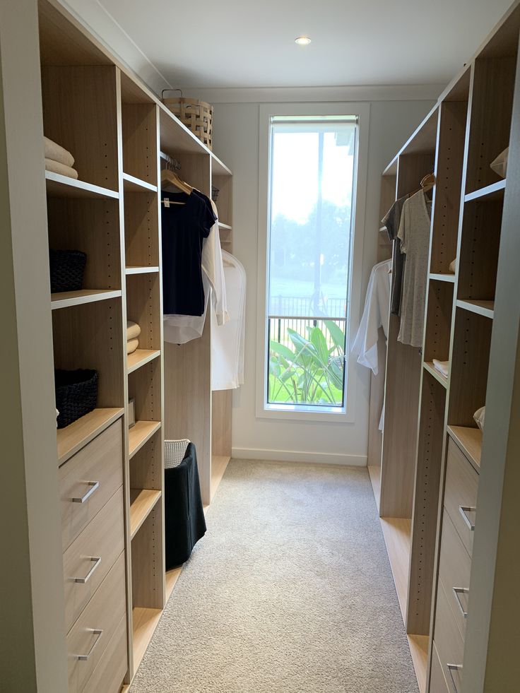 an empty walk in closet with lots of drawers and clothes on the shelves, next to a window