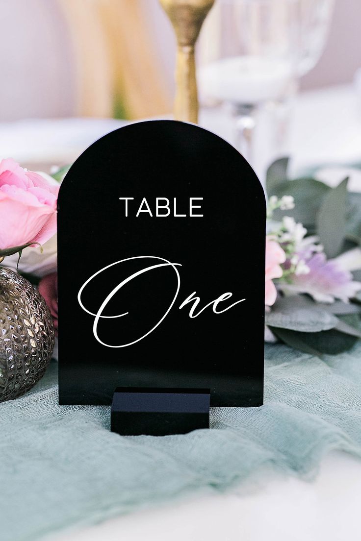 a black table number holder sitting on top of a blue table cloth with flowers in the background