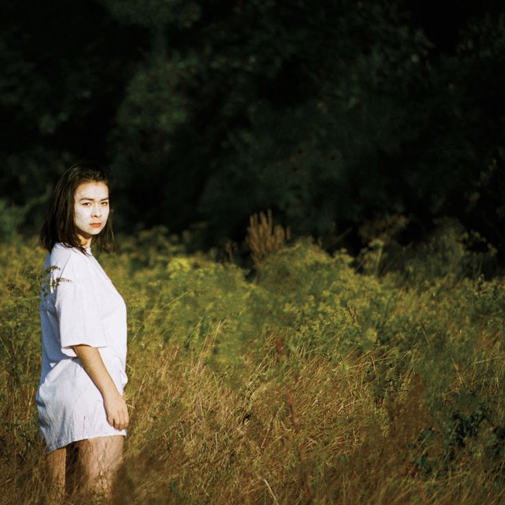 a woman standing in tall grass with trees in the background