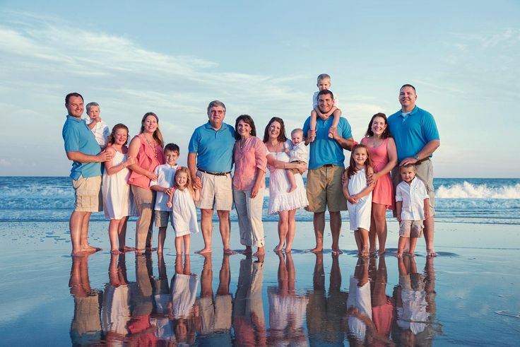 a large family is posing for a photo on the beach with their reflection in the wet sand