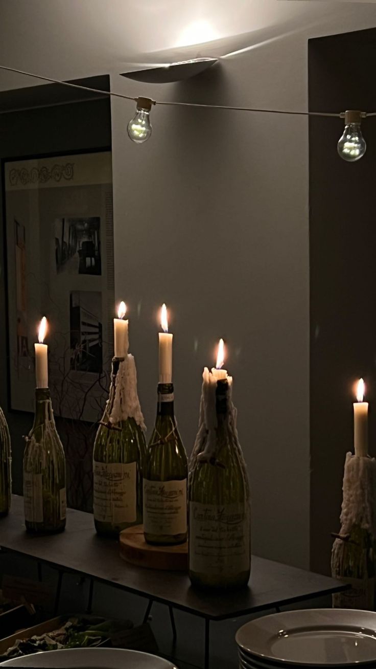 candles are lit in front of wine bottles on a table