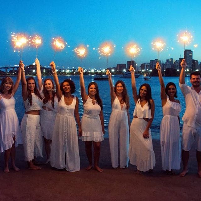 a group of women in white dresses holding sparklers over their heads at night by the water