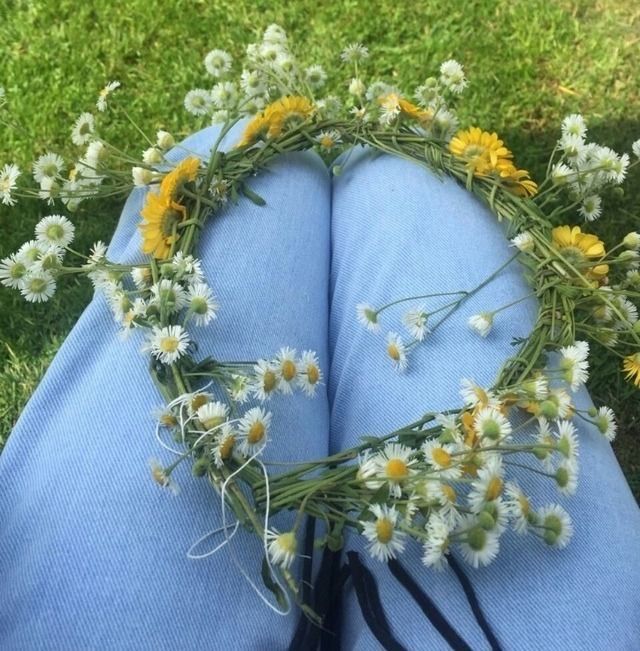 someone is laying on the grass with flowers in their lap and wearing a wreath made out of daisies