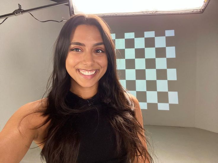 a woman in a black top is smiling for the camera with a checkered wall behind her