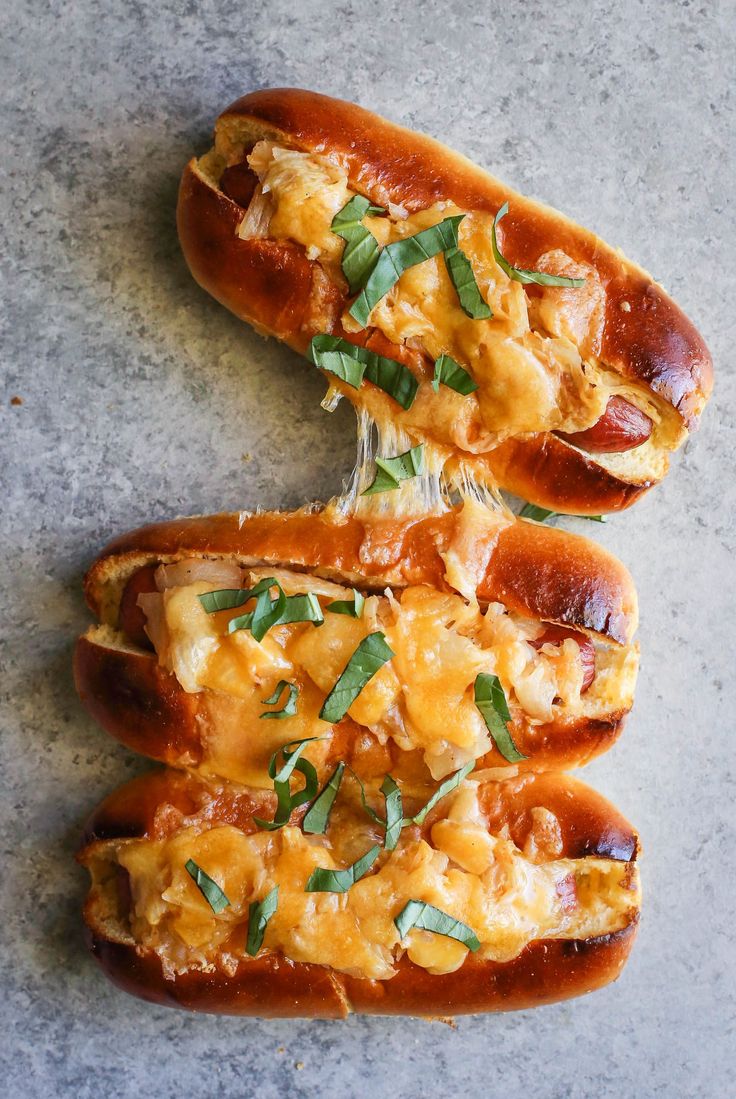 two hot dogs covered in cheese and toppings sitting on a counter top next to each other