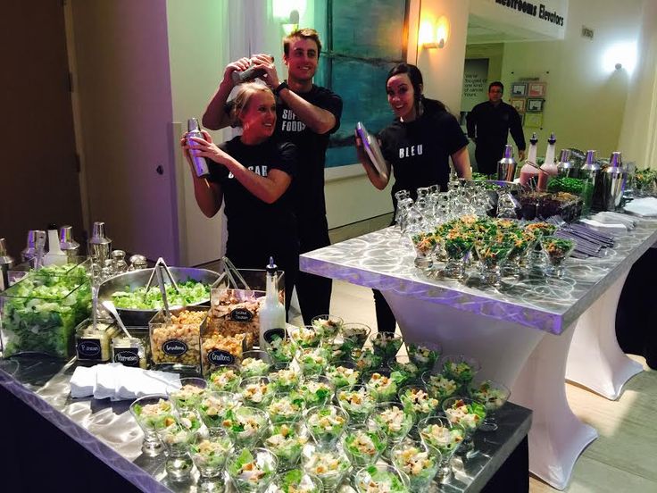 several people standing around a table full of food and drinks, all dressed in black t - shirts