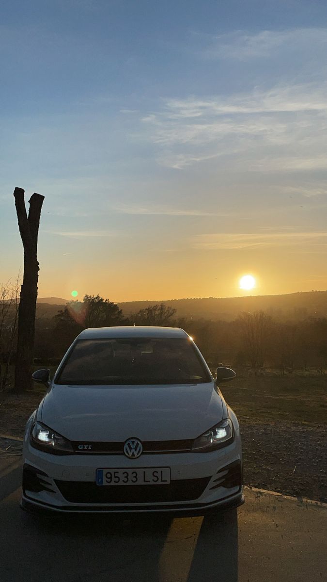 a white car parked on the side of a road near a tree at sunset or dawn