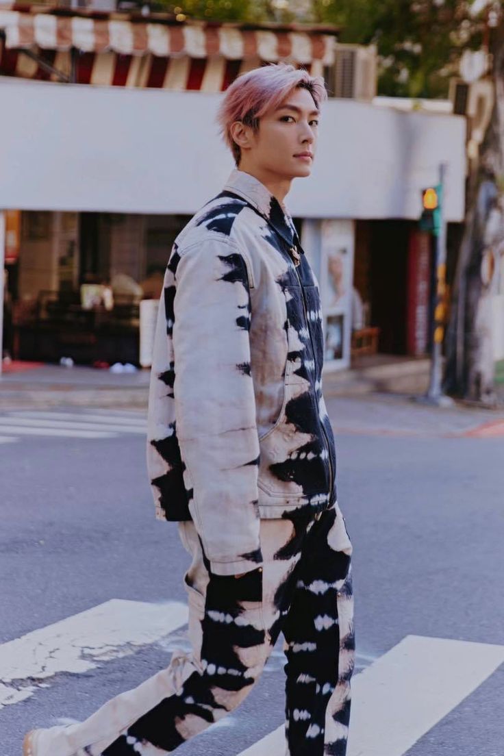 a man with pink hair is walking across the street wearing black and white clothing,