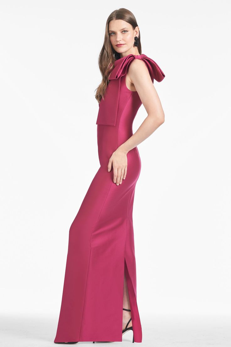 a woman in a long pink dress with a high neck and side slits, posing for