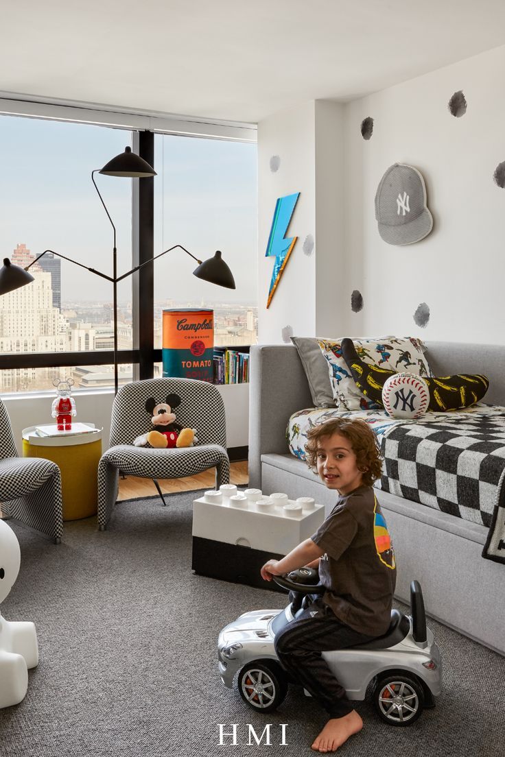 a young boy sitting on top of a toy car in a living room next to a window