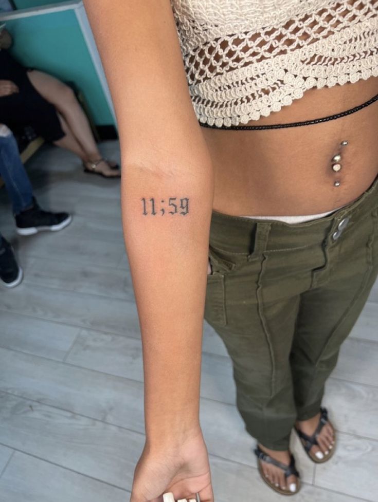 a woman with a small tattoo on her left arm and the number thirteen nine behind her